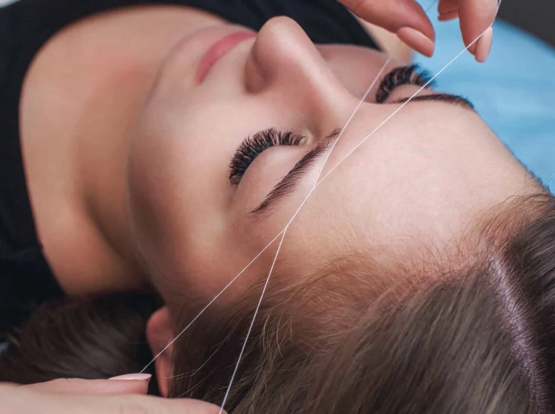 eyebrow threading vs waxing comparison at ny brows and beauty salon, showing a split-screen image with one side featuring a client receiving eyebrow threading and the other side showing a client getting eyebrow waxing. Both clients are in a professional salon setting with estheticians performing the respective treatments, highlighting the differences in technique and results between the two methods.
