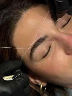 Esthetician shaping eyebrows with cotton thread in salon