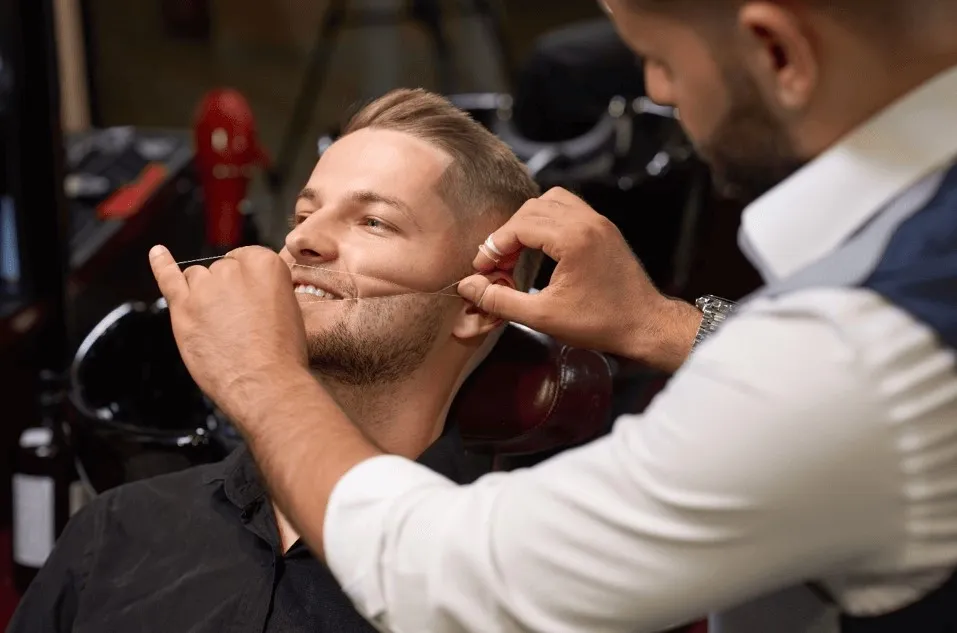 Skilled technician using cotton thread to separate unibrows and shape bushy eyebrows for men