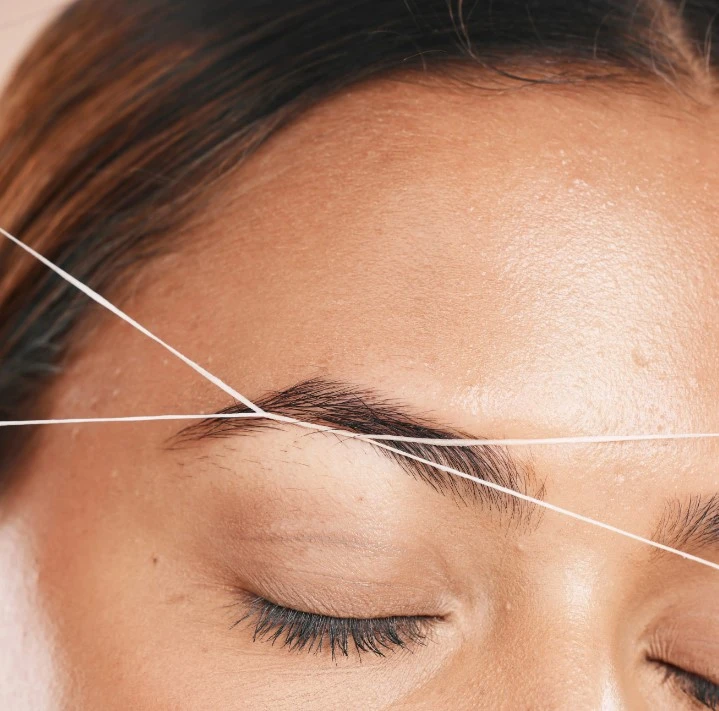Esthetician performing precise eyebrow threading and shaping for a bride